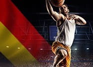 Ein Basketballspieler in Aktion und im Hintergrund die deutsche Flagge.