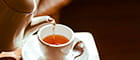 Eine Tasse wird mit einer Kanne mit Tee gefüllt.
