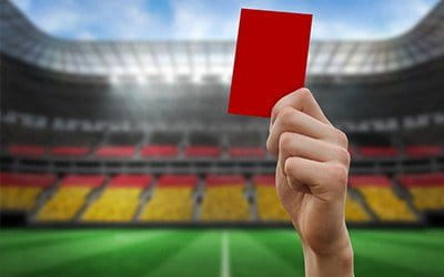 Eine Rote Karte wird gezeigt und im Hintergrund ein Stadion.